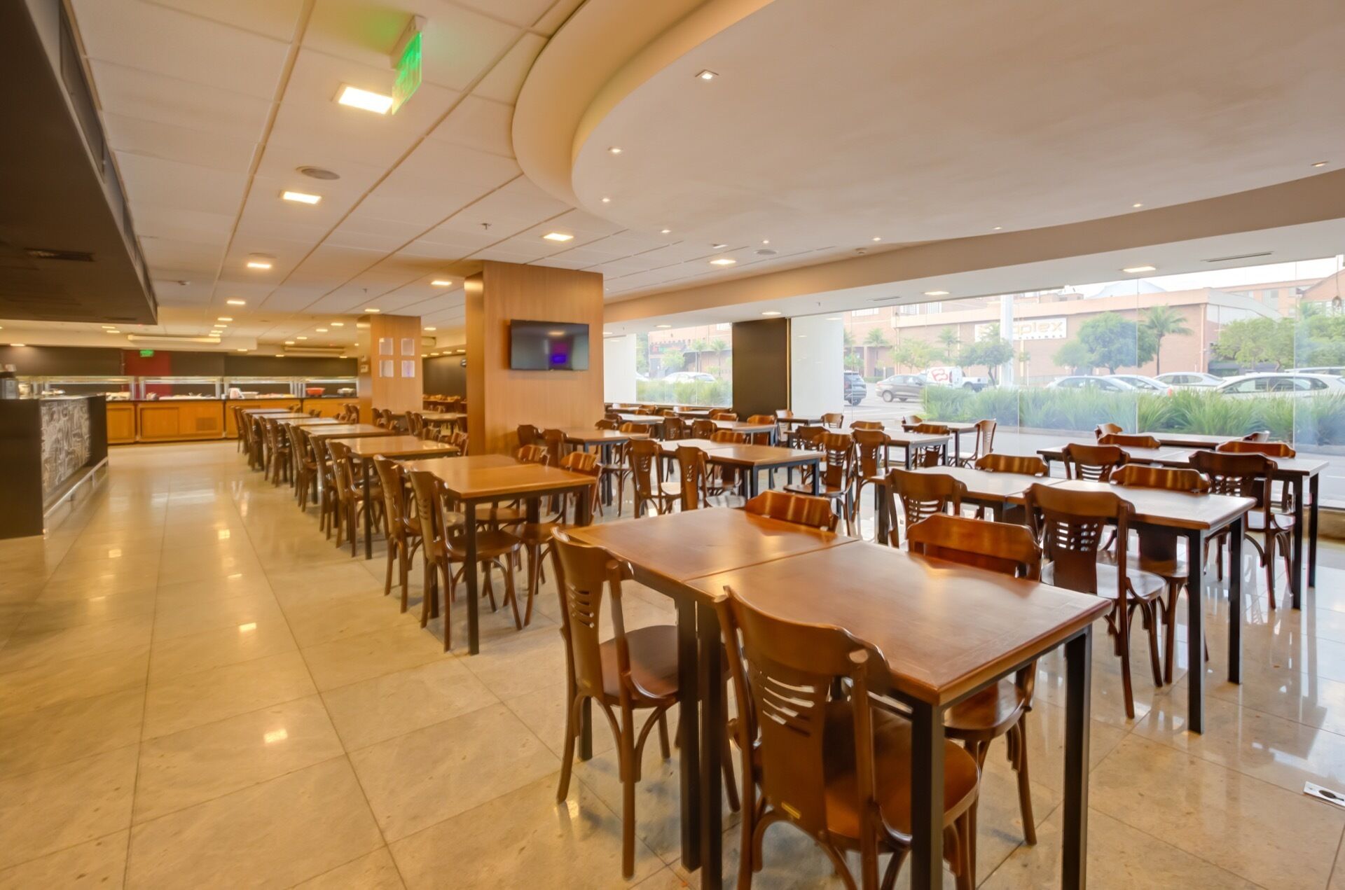 A spacious restaurant with multiple dining tables and chairs, a counter with a menu display, and large windows offering a view of the street.