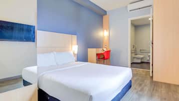 Quarto de hotel com cama, escrivaninha, cadeira, banheiro e armário.