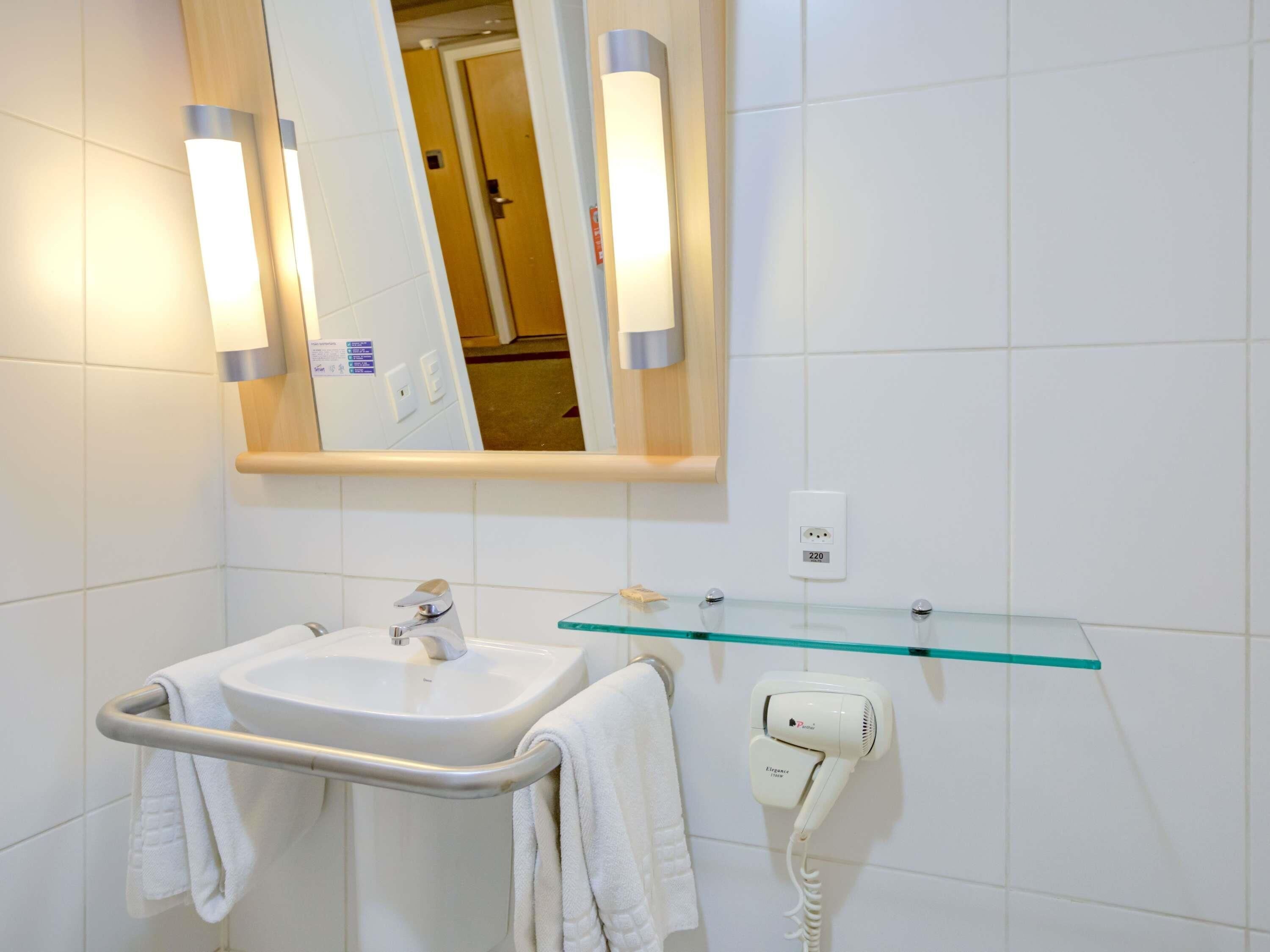 A bathroom with a sink, mirror, towel rack, glass shelf, and a hairdryer.