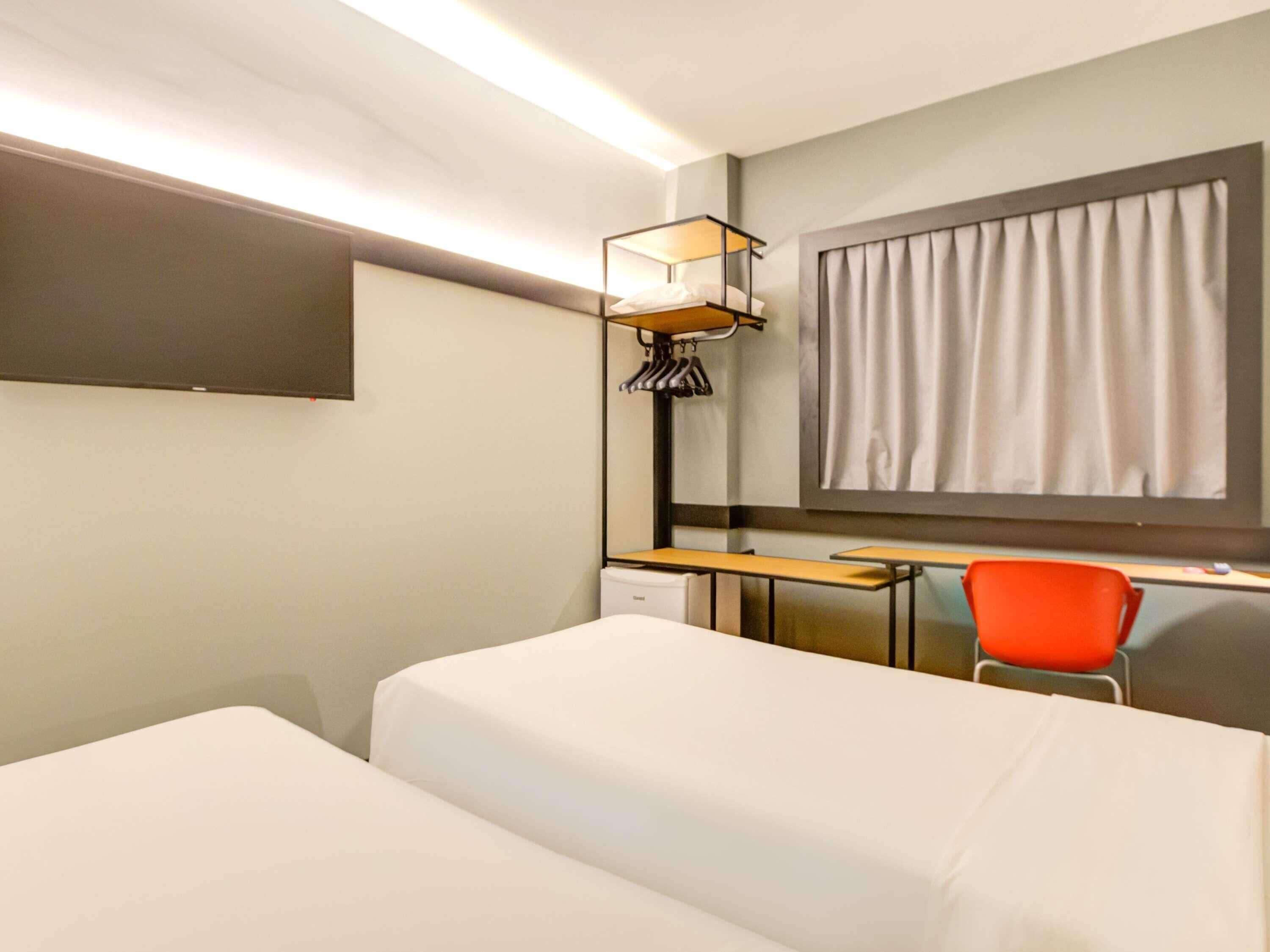 A hotel room with a bed, desk, chair, and a window with curtains.