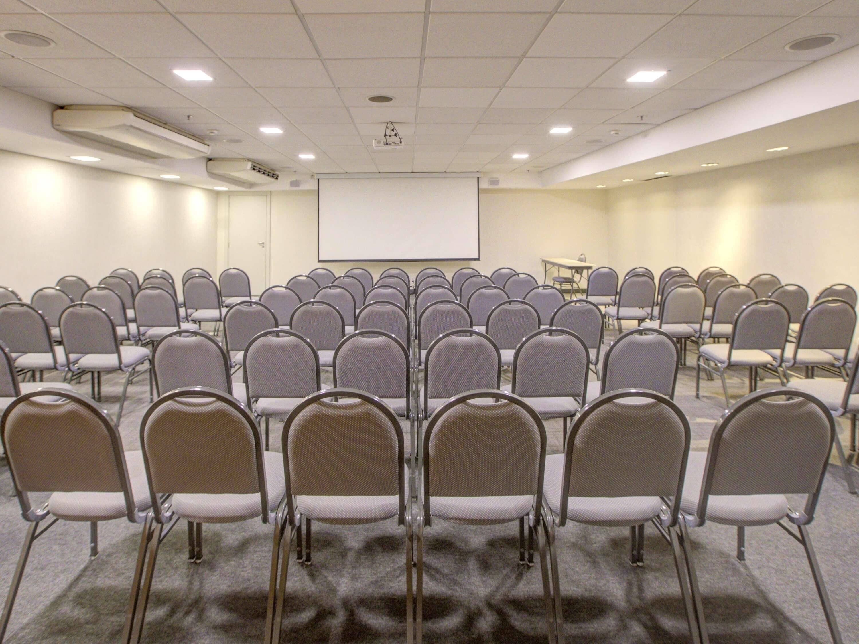 A conference room with rows of chairs, a projector screen, and a carpeted floor.