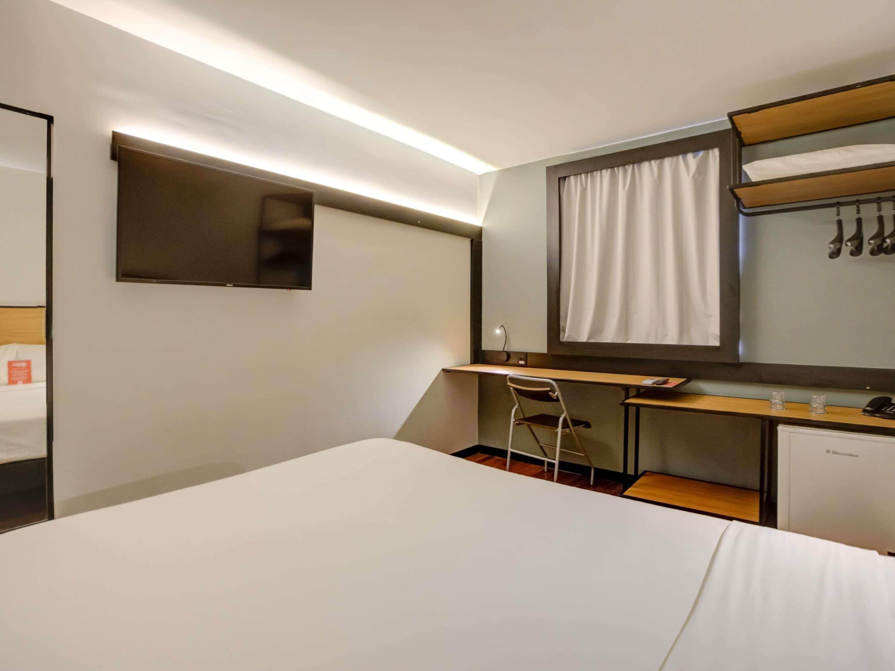 Una habitación de hotel con cama, escritorio, silla, televisor y espejo.