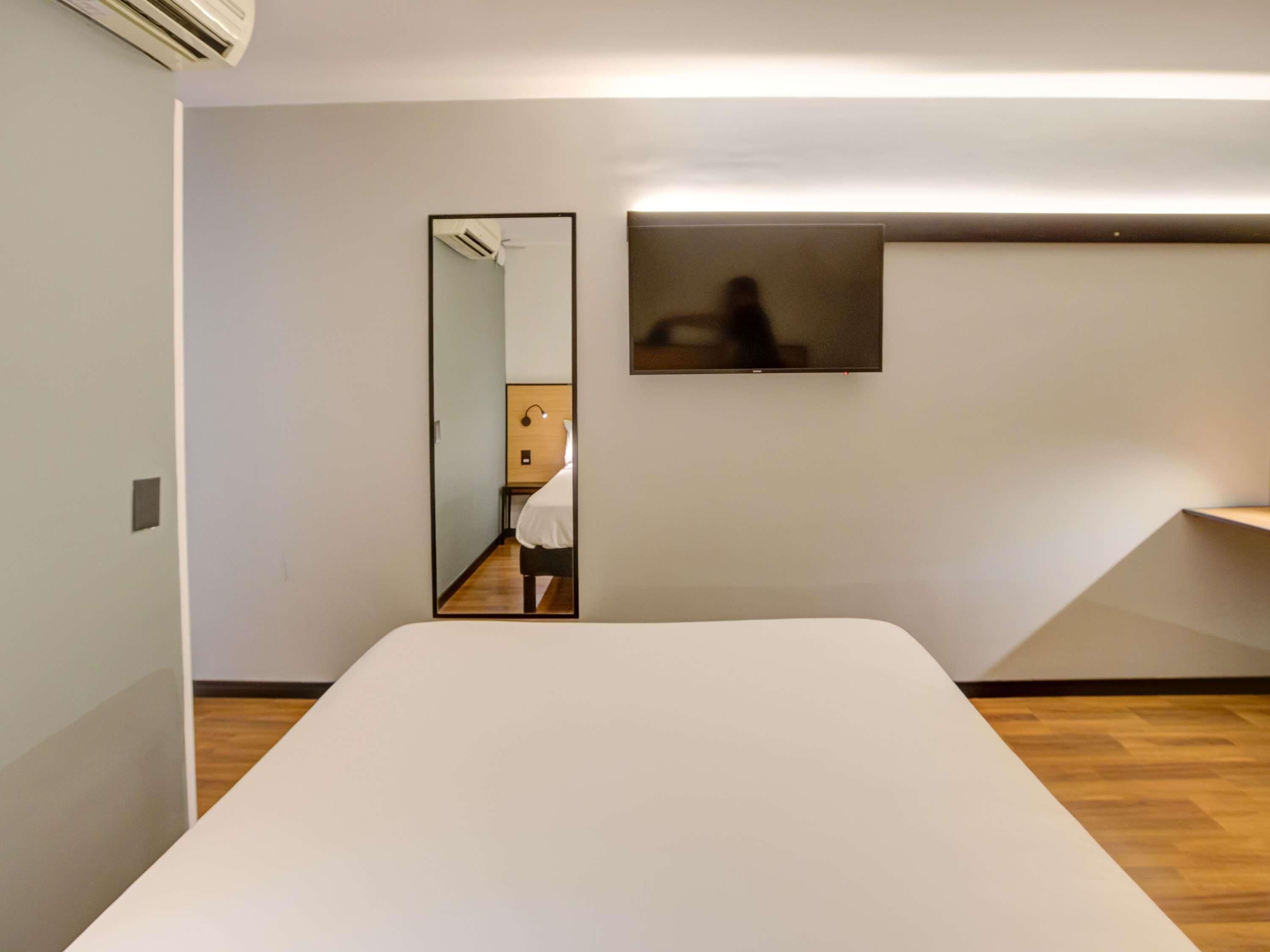 Een moderne hotelkamer met een groot bed, een zithoekje, een spiegel en een televisie.