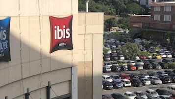 Un hotel con un llamativo letrero rojo de Ibis, un estacionamiento con varios coches y una vista despejada del paisaje urbano al fondo.