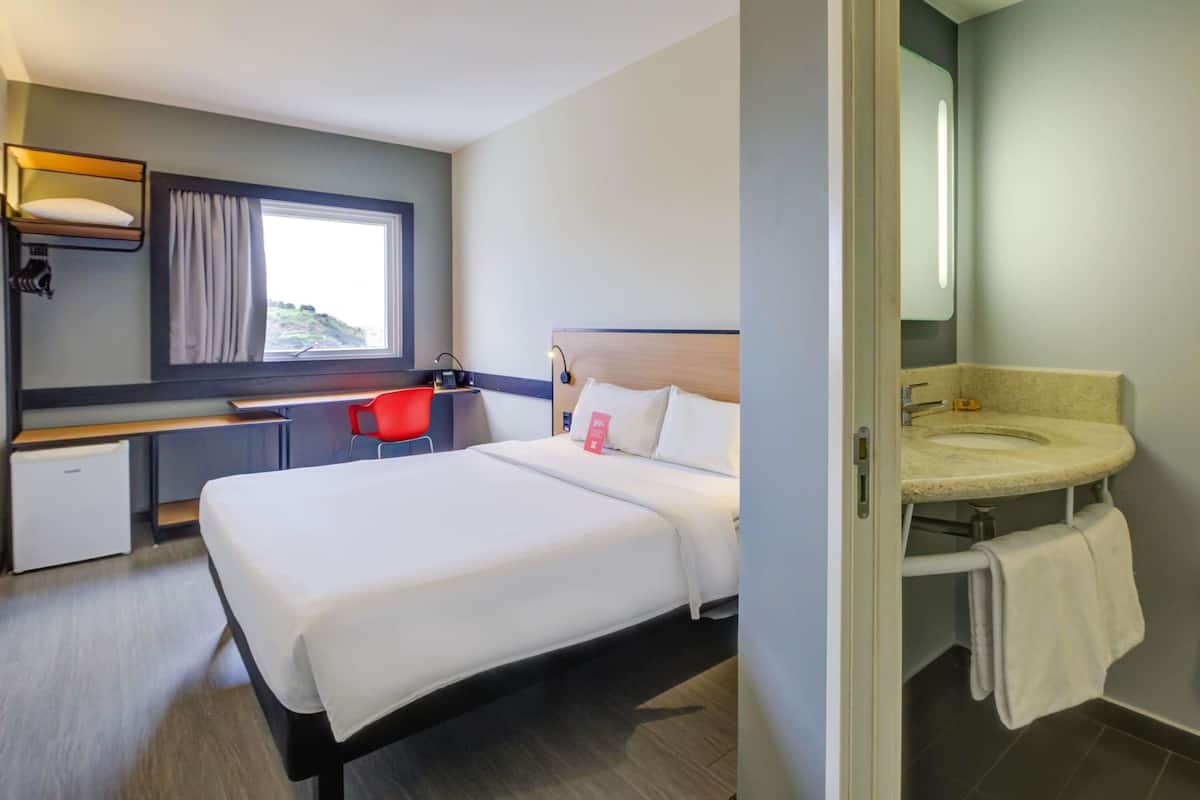 Ein Hotelzimmer mit Bett, Schreibtisch, Stuhl, einer kleinen Küchenzeile und einem Badezimmer.
