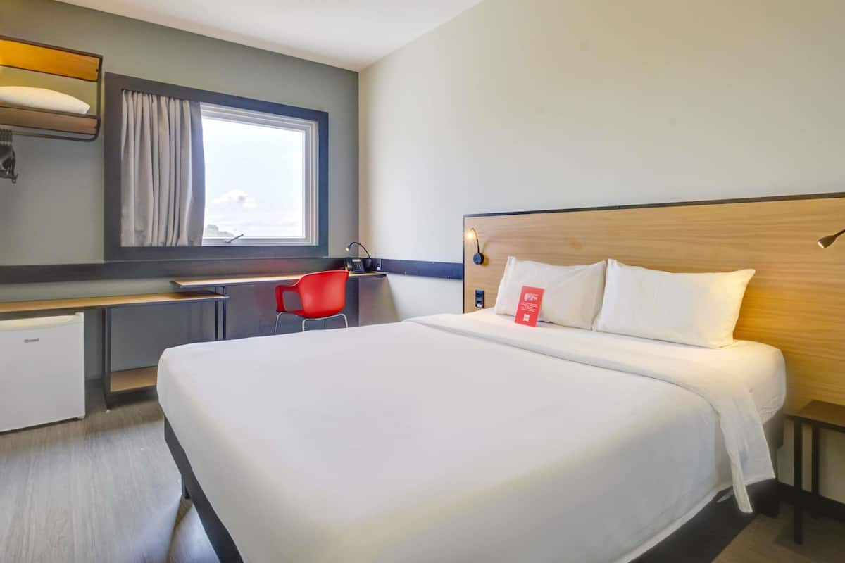 Ein Hotelzimmer mit einem großen Bett, einem Schreibtisch, einem Stuhl und einem fenster mit Vorhängen.