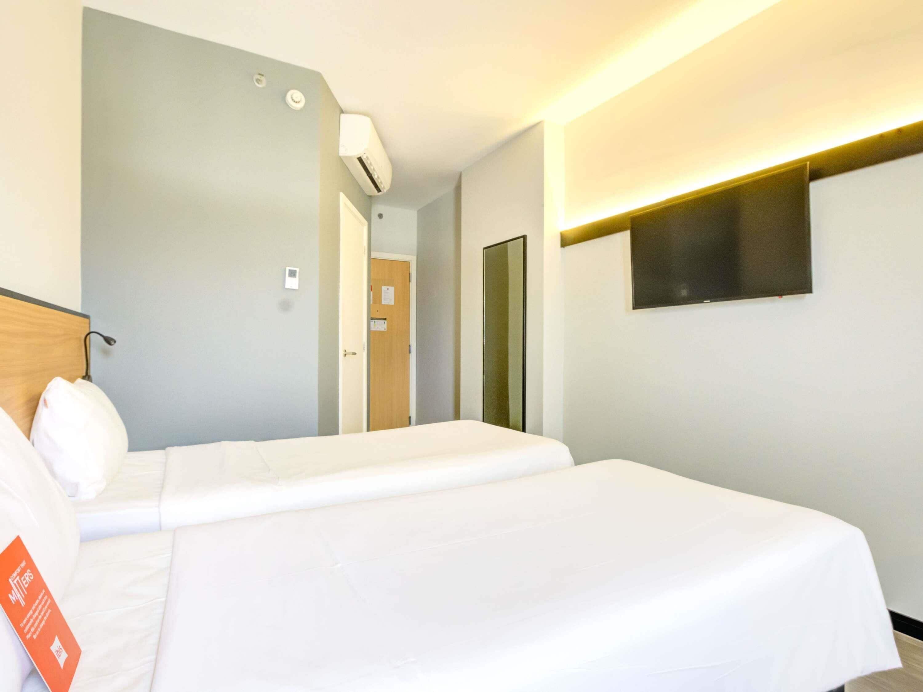 A hotel room with a bed, a bedside table, a mirror, and a wall-mounted TV.