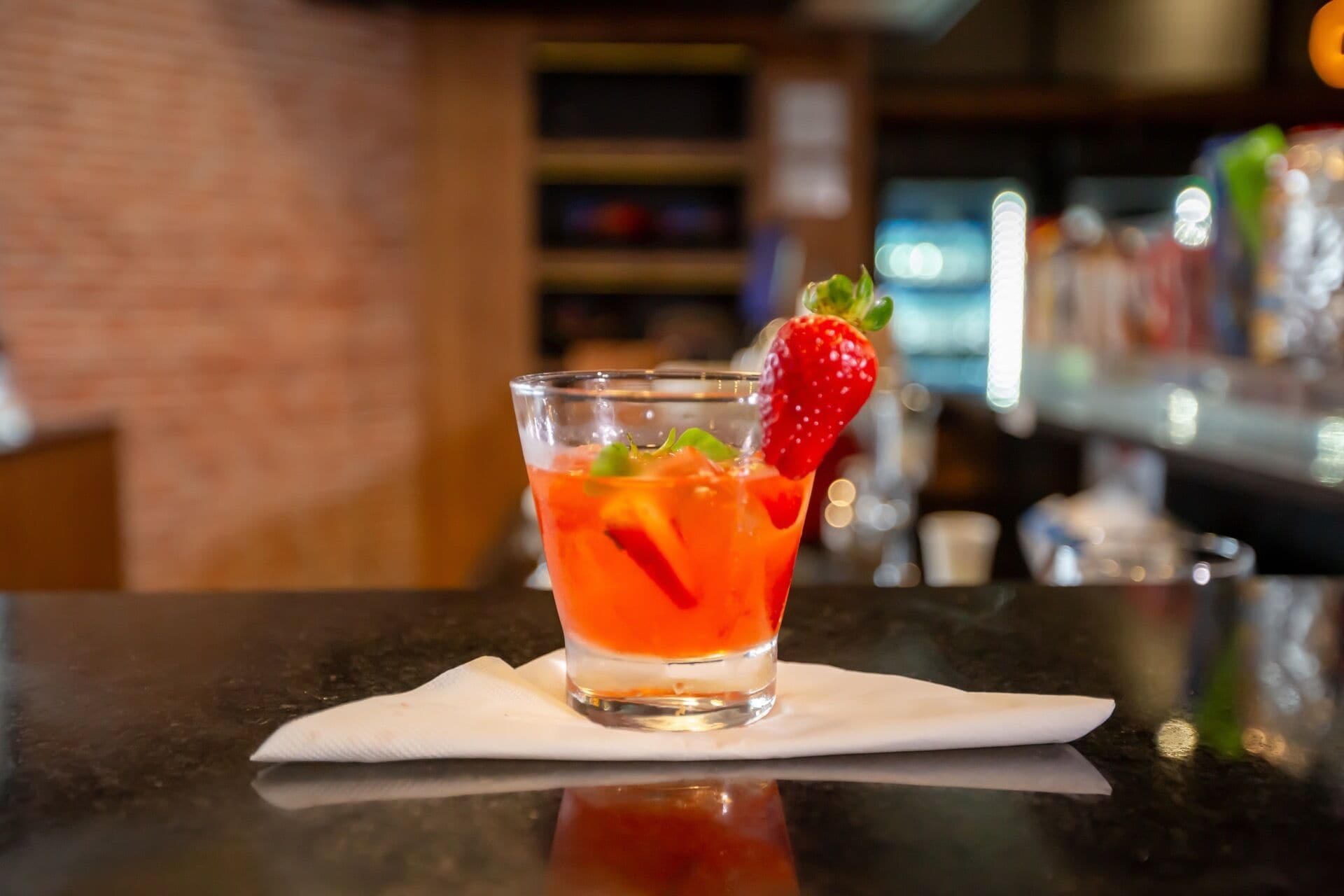 A glass of red cocktail with a strawberry garnish on a bar counter.