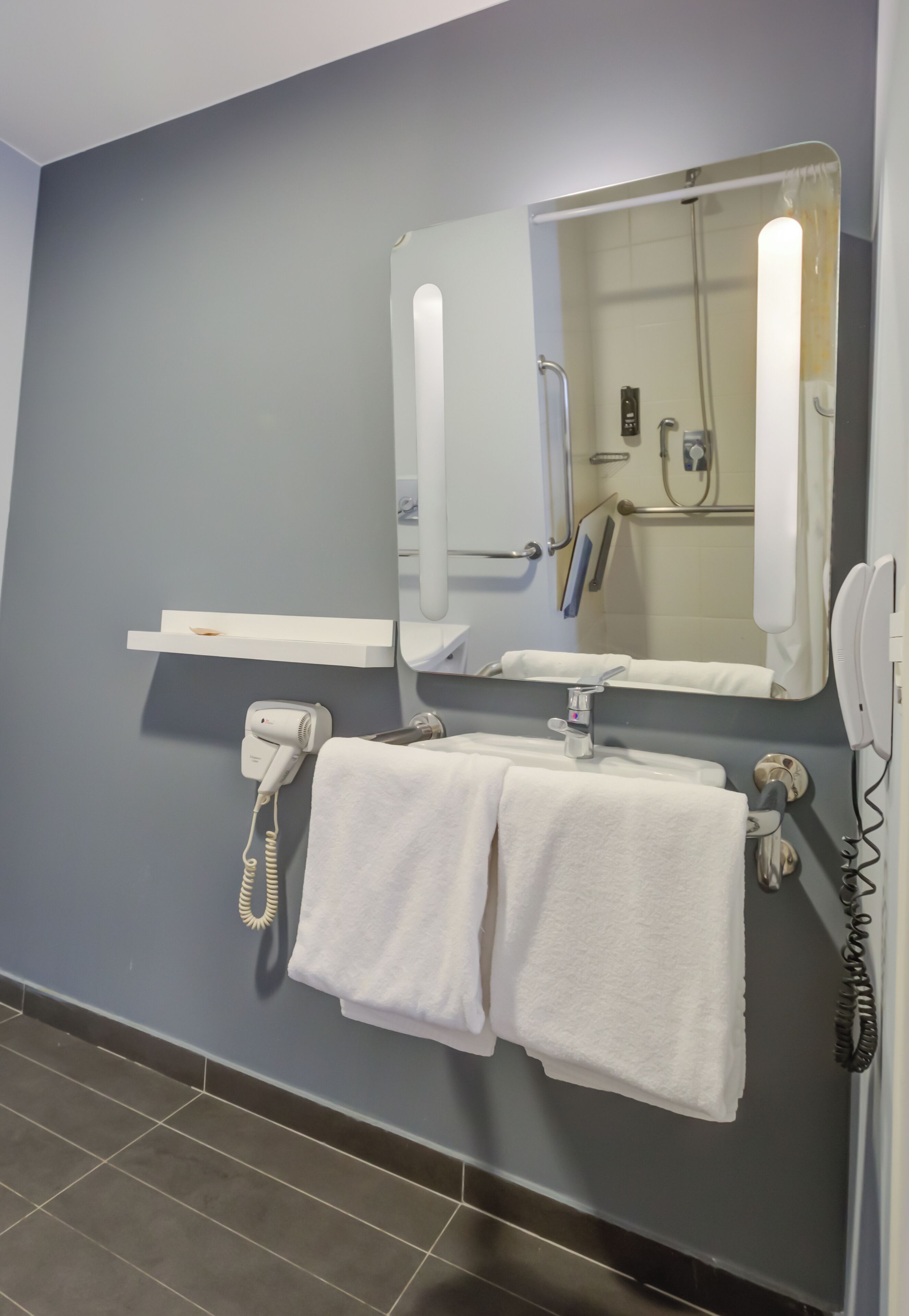 Un baño con espejo, secador de pelo, toallero y zona de ducha.