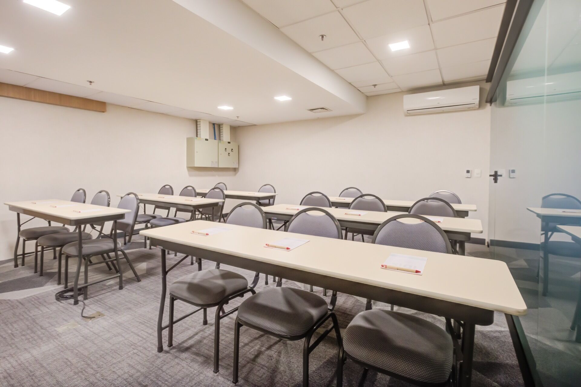 Un salón de conferencias con varias mesas y sillas, una pizarra y un equipo de aire acondicionado en la pared.