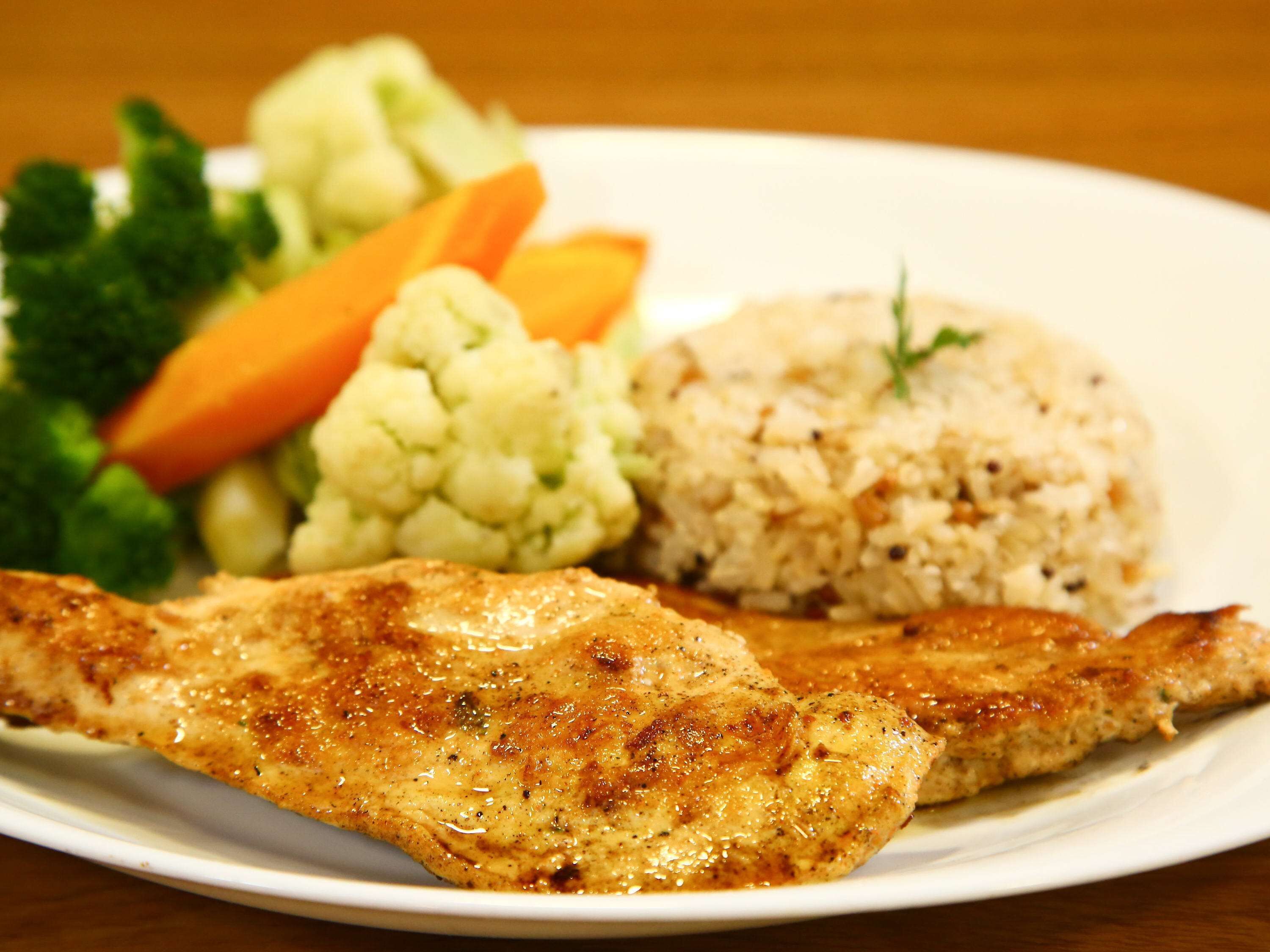 A plate with grilled chicken, rice, and vegetables including carrots and cauliflower.