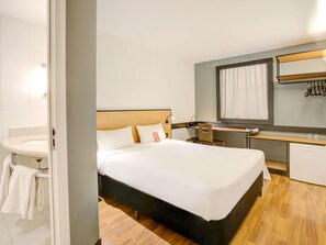 A hotel room with a bed, a desk, a chair, a small kitchenette, and a bathroom.