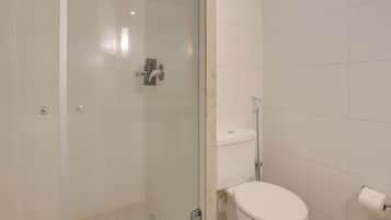 Un baño con ducha de mampara de vidrio, inodoro y rollo de papel higiénico.