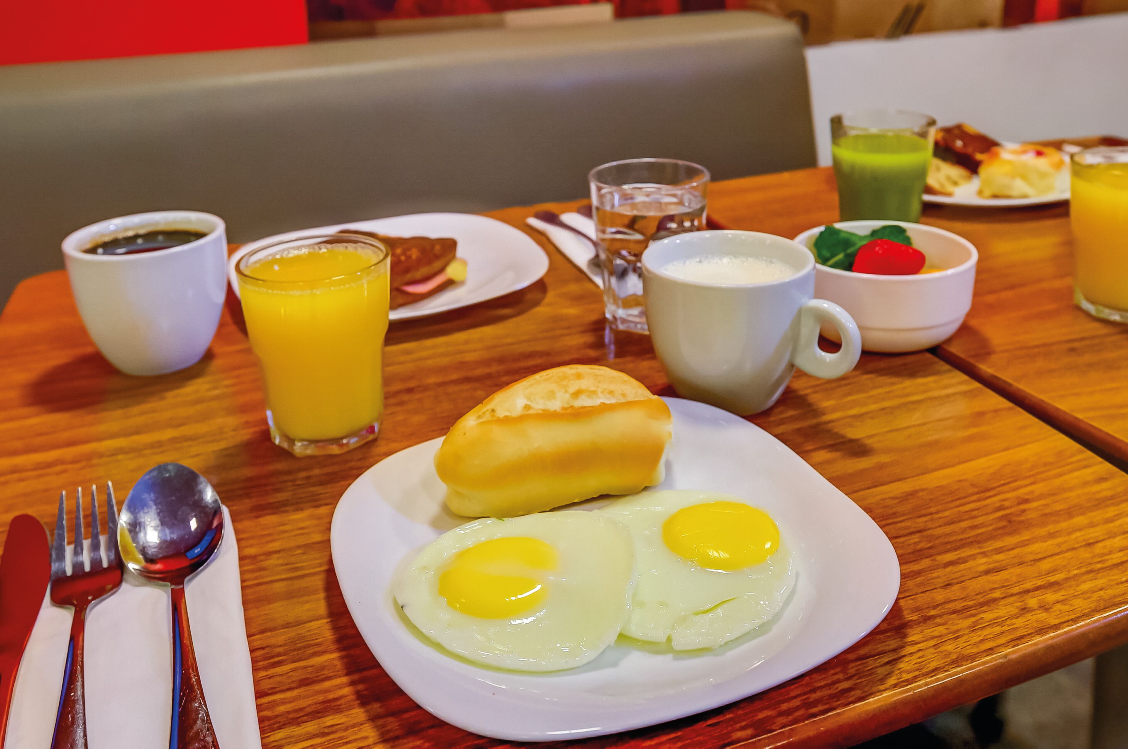 Disposição para o café da manhã com um prato de ovos, um pão e um copo de suco de laranja sobre uma mesa de madeira.
