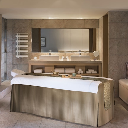 A modern bathroom with a large mirror, two sinks, a heated towel rail, and a bed with a large towel.