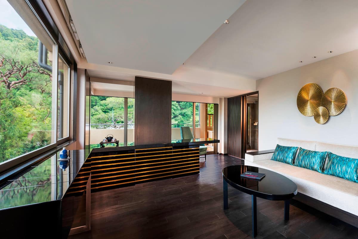 A modern living room with a large window, a sofa, a coffee table, and a decorative wall piece.