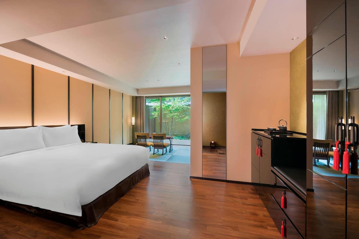 A modern hotel room with a large bed, a dining area, and a kitchen.