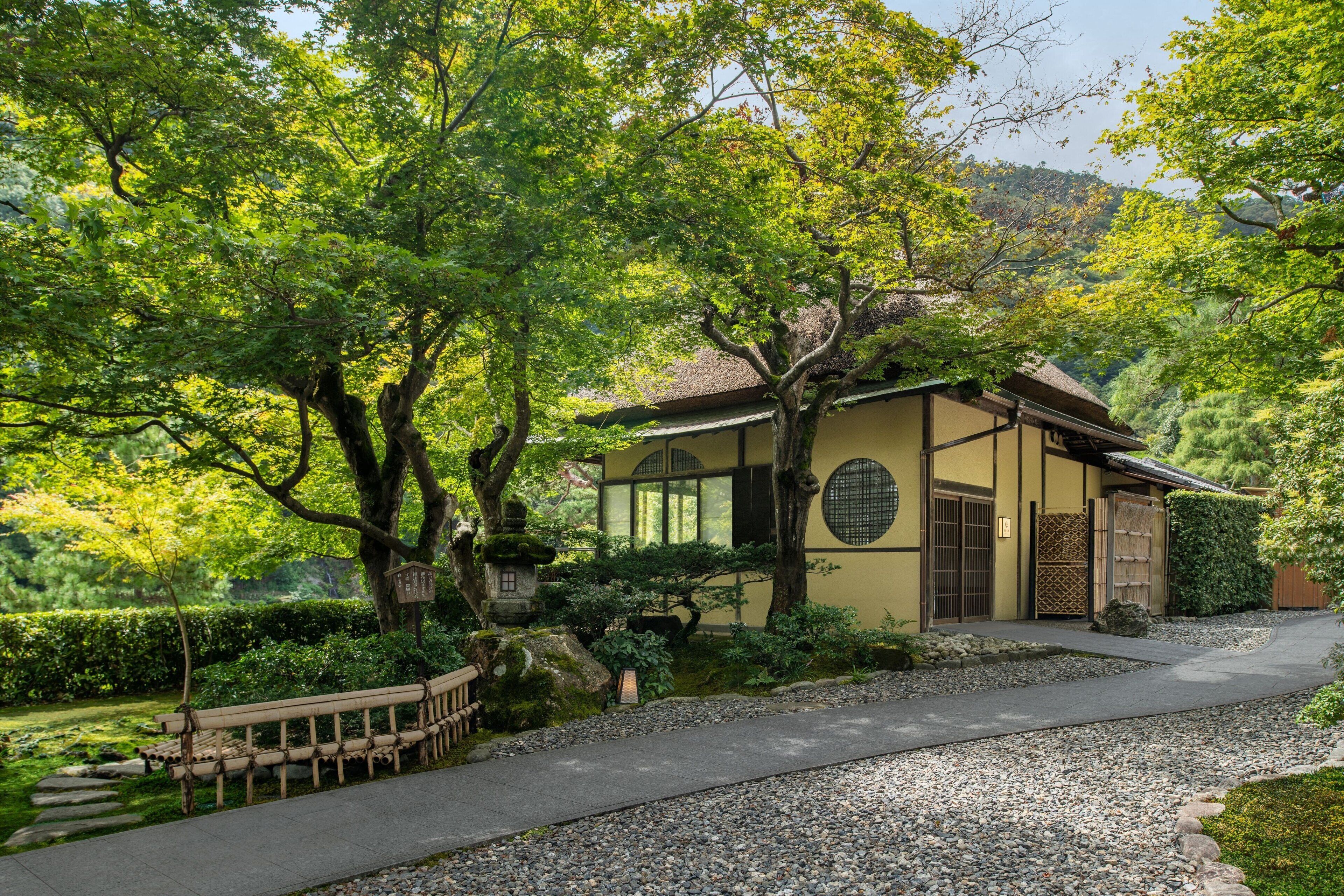 Un edificio japonés tradicional rodeado de exuberante follaje y un sendero de grava.