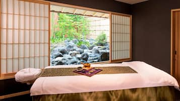 A room with a tatami mat bed, a window with shoji screens, and a view of a rock garden.