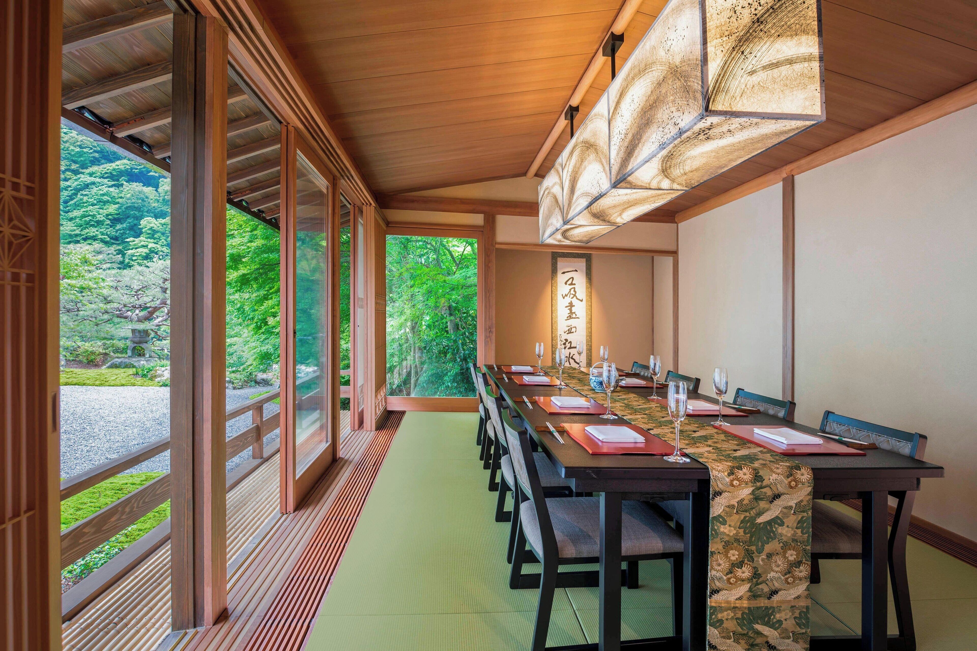 Comedor japonés tradicional con esteras de tatami, una mesa larga dispuesta para una comida y vistas a un exuberante jardín a través de amplios puertas correderas.