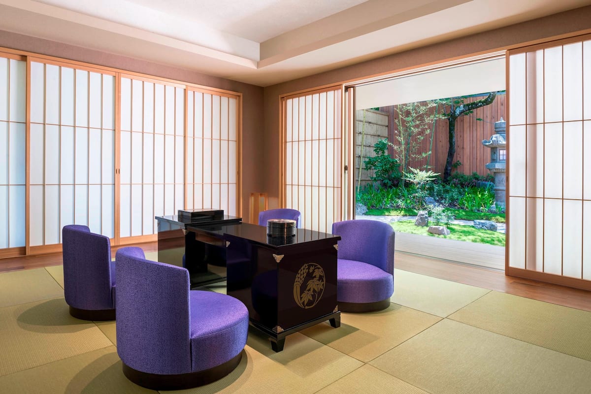 A traditional Japanese room with tatami flooring, a low table, purple chairs, and sliding doors leading to a garden.