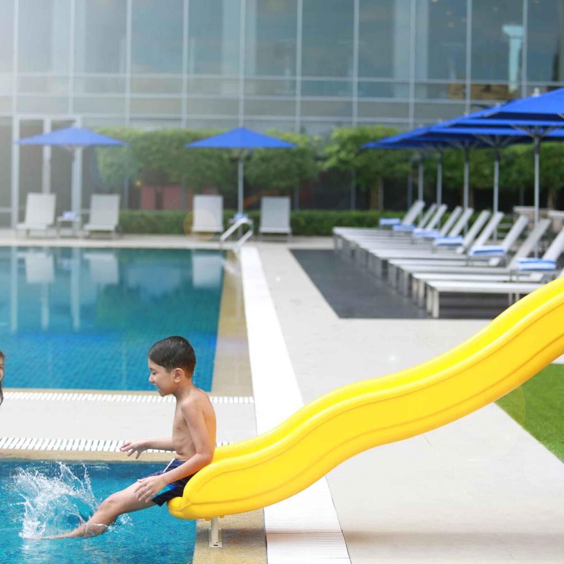 Ein Swimmingpool mit gelb rutschendem Element, Liegestühlen und Sonnenschirmen.