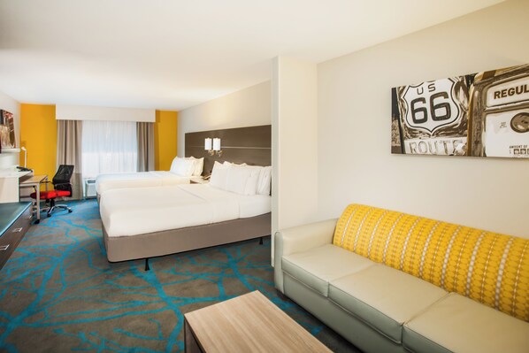 Quarto de hotel com duas camas, um sofá, uma escrivaninha e uma cadeira.