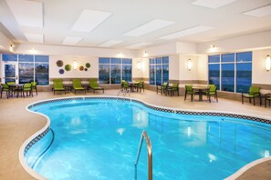 An indoor swimming pool with a tiled edge, surrounded by green chairs and tables, and large windows with a view. - Holiday Inn Express & Suites Litchfield West by IHG (Litchfield)