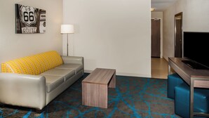 A modern hotel room with a gray sofa, a wooden coffee table, a TV, and a patterned carpet. - Holiday Inn Express & Suites Litchfield West by IHG (Litchfield)