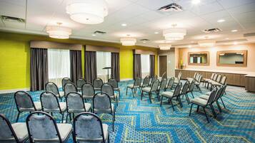 Un salón de conferencias con filas de sillas, un amplio ventanal con cortinas y suelo alfombrado.