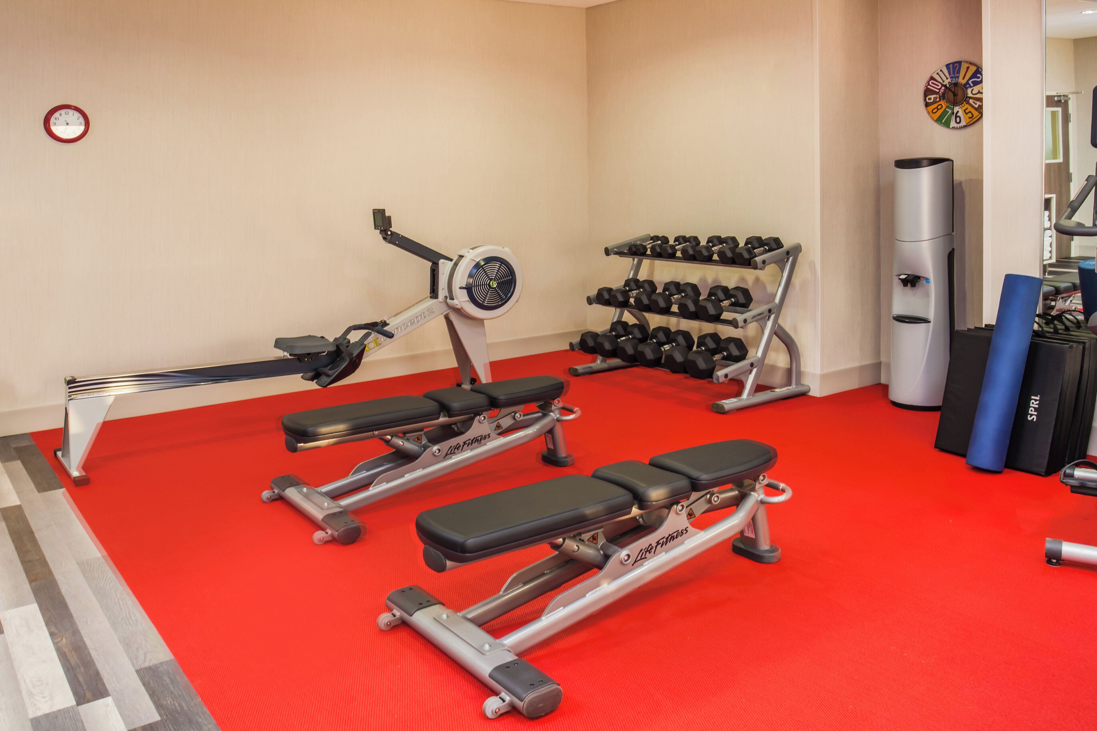 Un gimnasio con equipo de ejercicio, incluyendo una máquina de remo, mancuernas y bancos.
