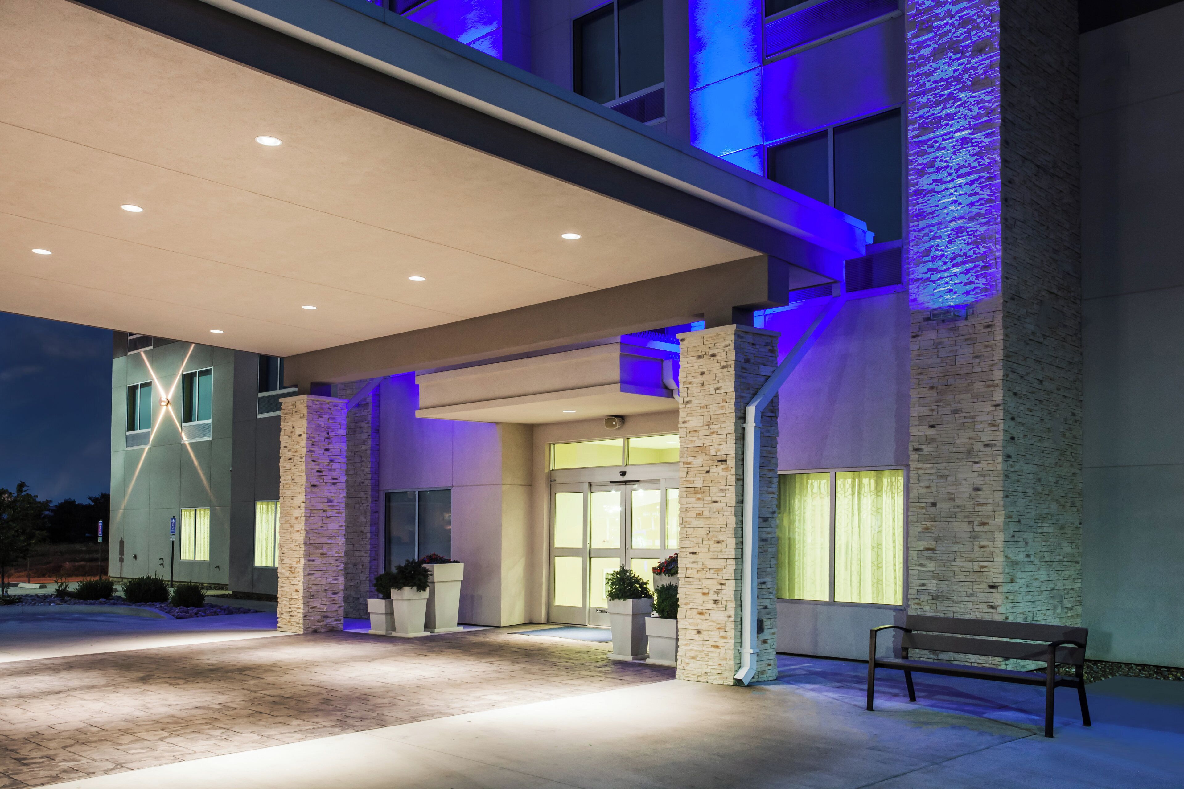 A building with a covered entrance, stone pillars, and a bench outside.