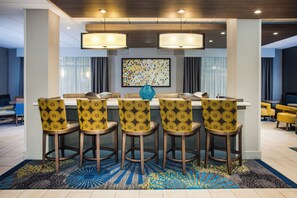 A hotel dining area with a long table, six chairs with patterned upholstery, and a large abstract painting on the wall. - Holiday Inn Express & Suites Litchfield West by IHG (Litchfield)