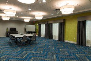 A conference room with a blue patterned carpet, a white table with chairs, a projector screen, and curtains on the windows. - Holiday Inn Express & Suites Litchfield West by IHG (Litchfield)