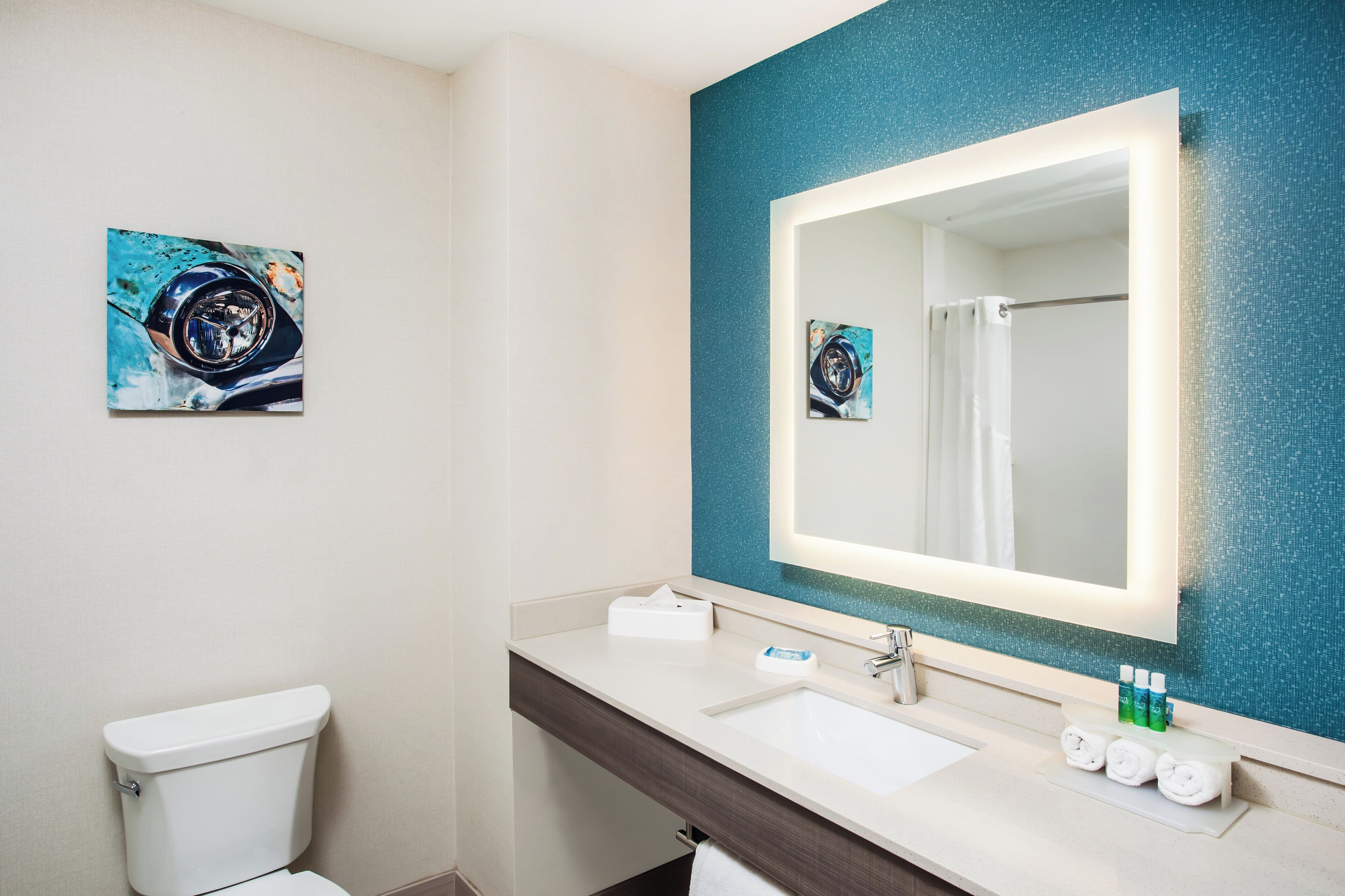 A bathroom with a white toilet, a sink with a mirror, and a blue textured wall.