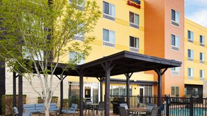 Exterior de un hotel con mesas al aire libre, un patio cubierto y una piscina.