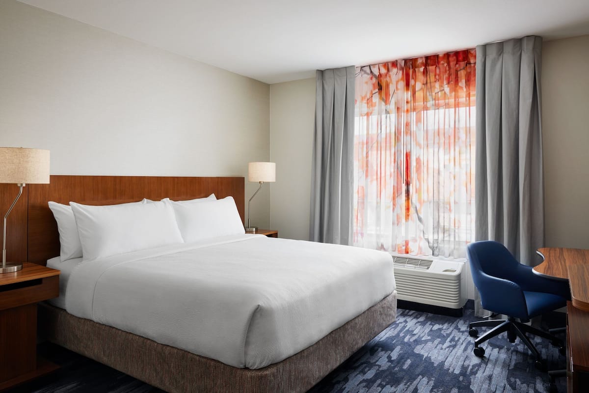 Une chambre d’hôtel avec un grand lit, un bureau, une chaise, une lampe et une fenêtre avec des rideaux.