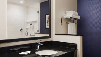 A bathroom with a black countertop, a white sink, and a large mirror. There are towels on a shelf and a framed picture on the wall.