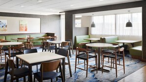 Un comedor de hotel con mesas redondas, sillas y asientos acolchados verdes.