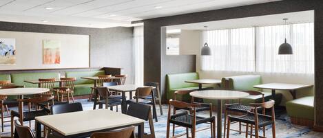 Un comedor de hotel con mesas redondas, sillas y asientos acolchados verdes.