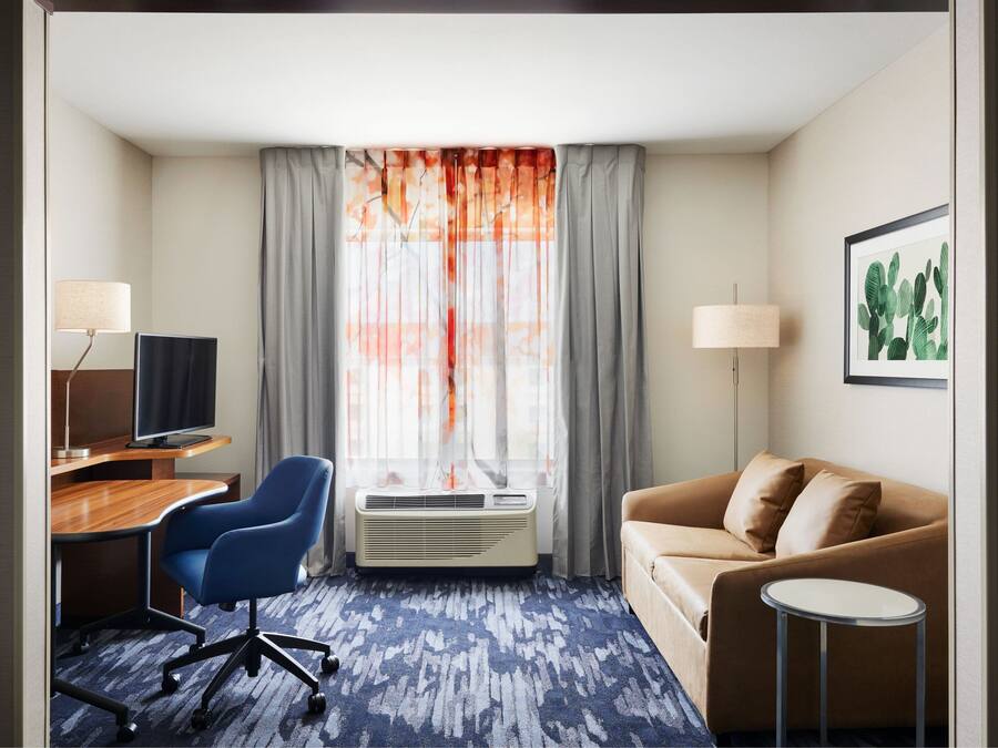 A hotel room with a desk, chair, air conditioning unit, sofa, and a small table.