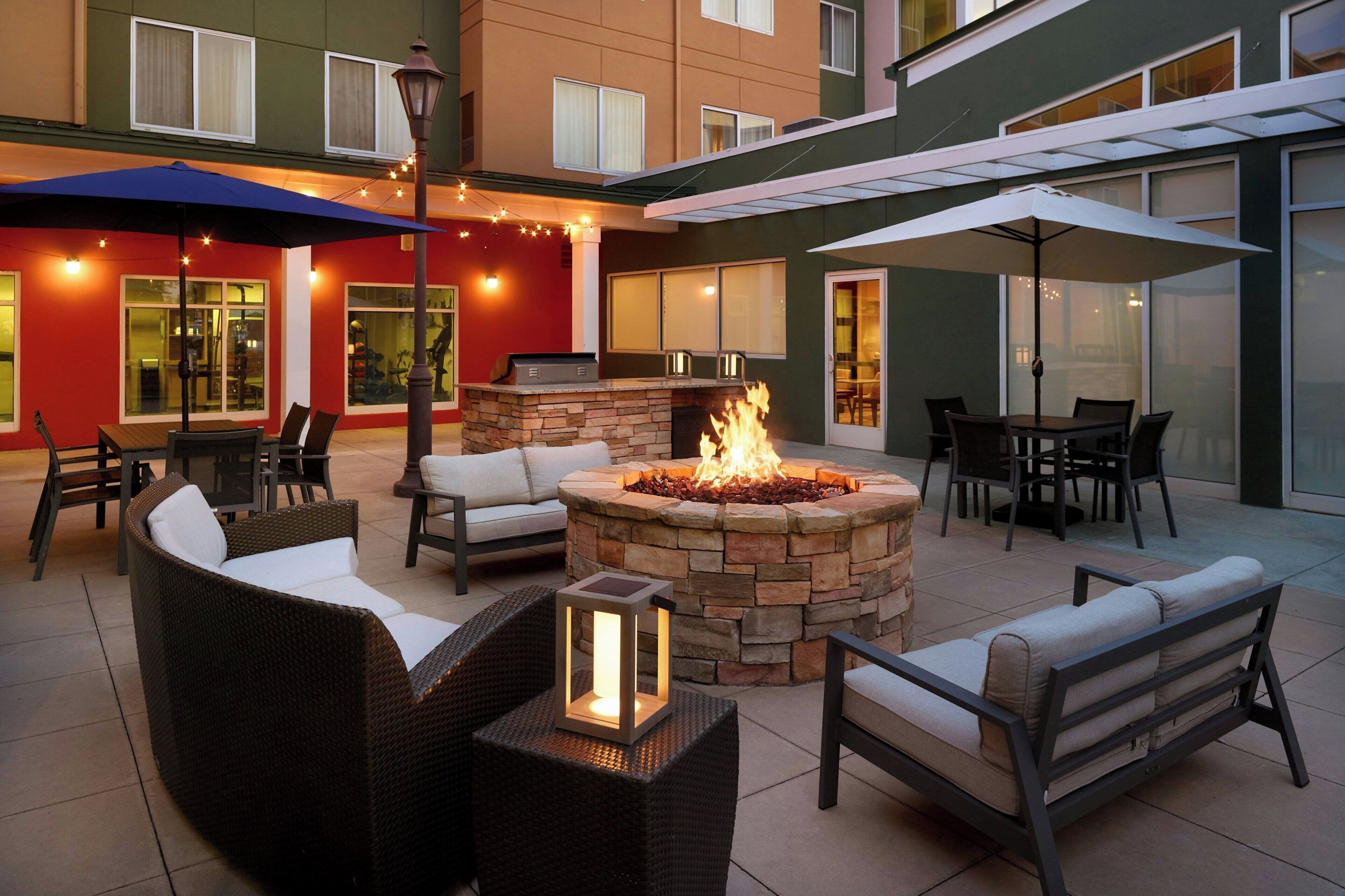 An outdoor patio area with a stone fire pit, wicker furniture, and umbrellas providing shade.