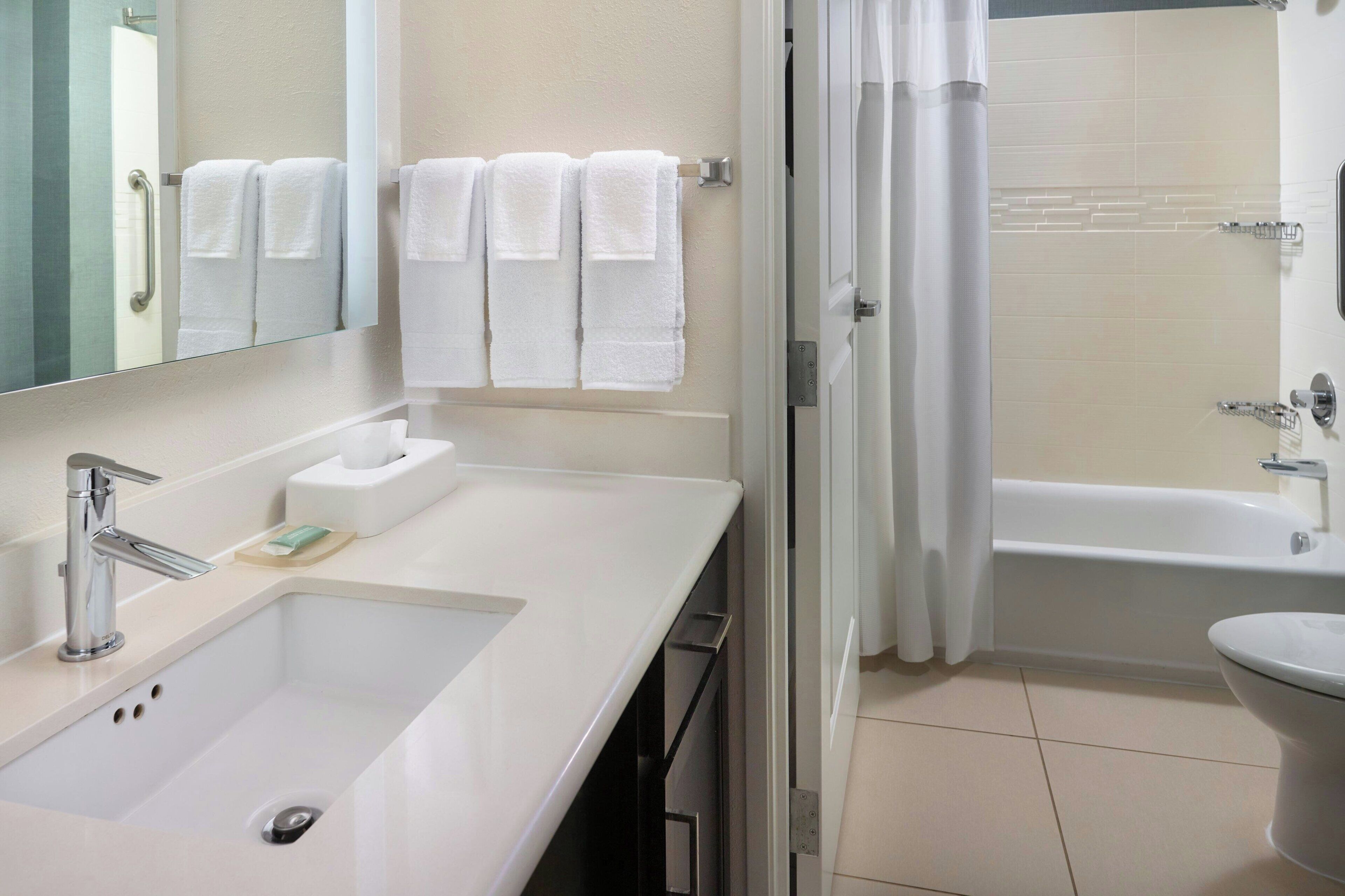 A bathroom with a sink, mirror, towel rack, and a shower area.