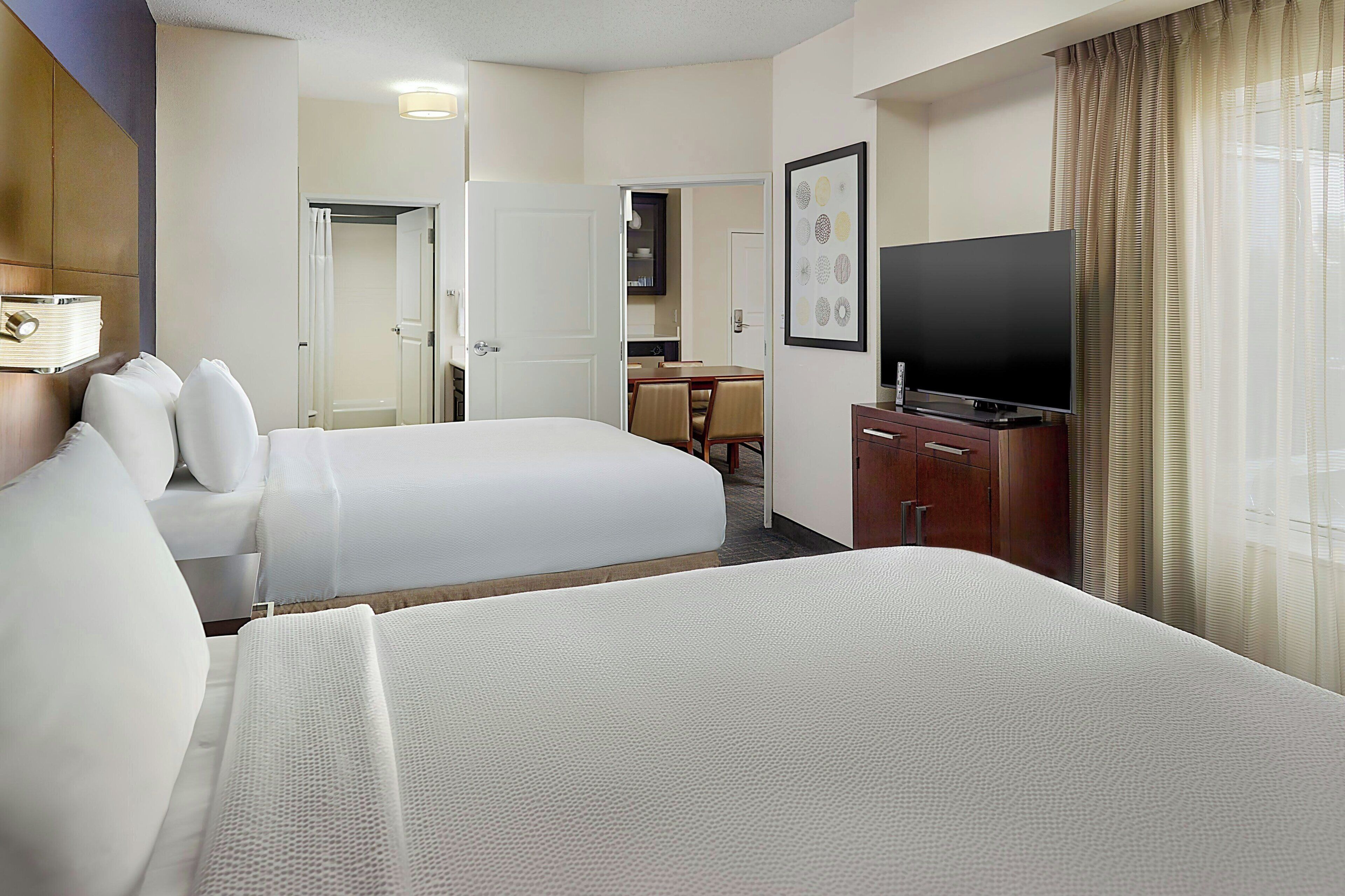 A hotel room with two beds, a television, a desk, and a bathroom.
