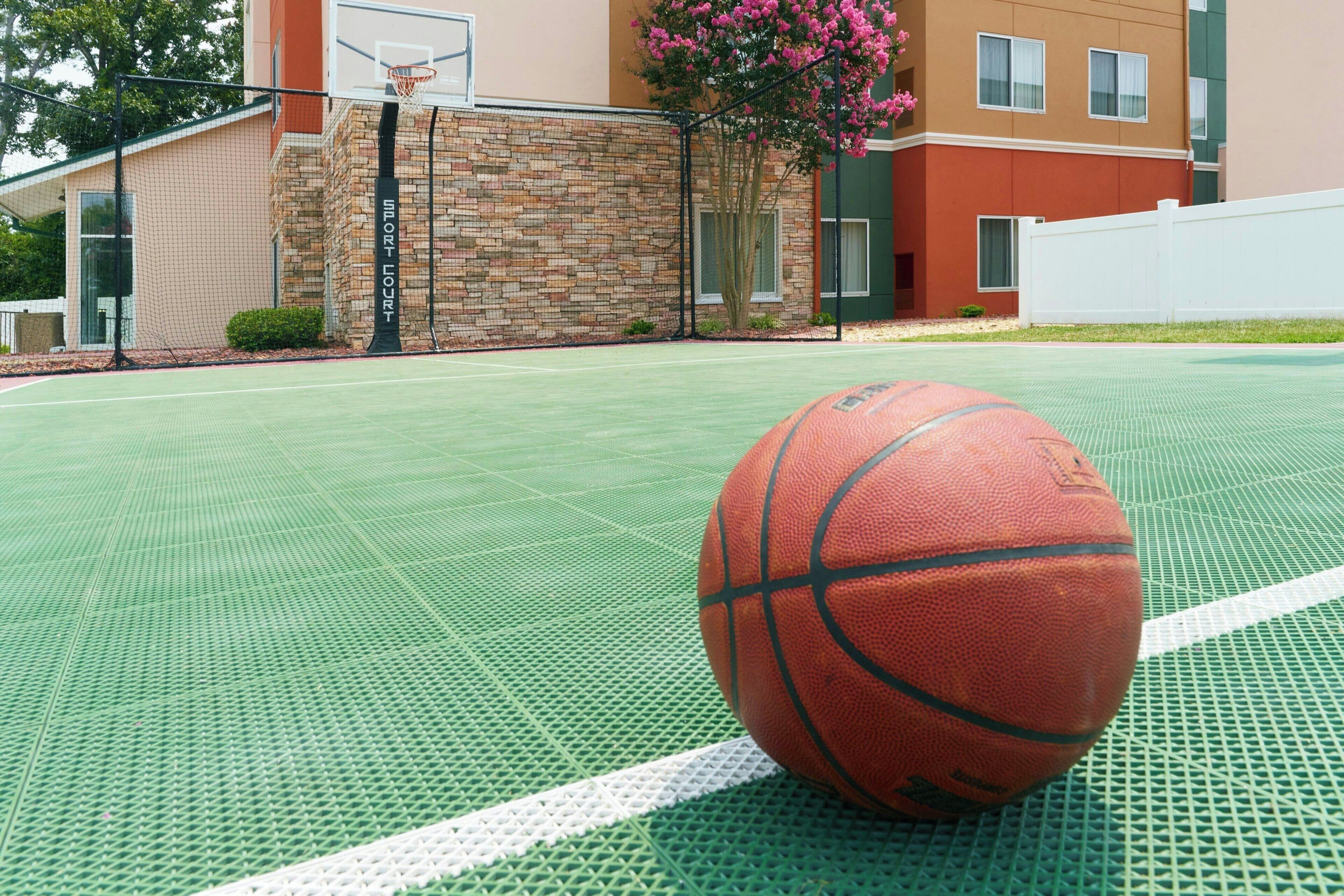 A basketball court with a ball, a brick wall, and a building with windows and a door.