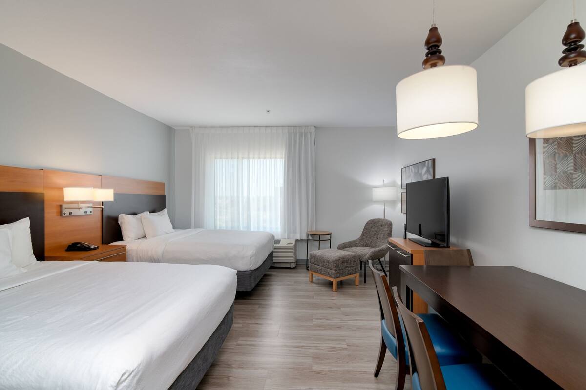 A hotel room with two beds, a desk, a chair, a television, and a large window with curtains.