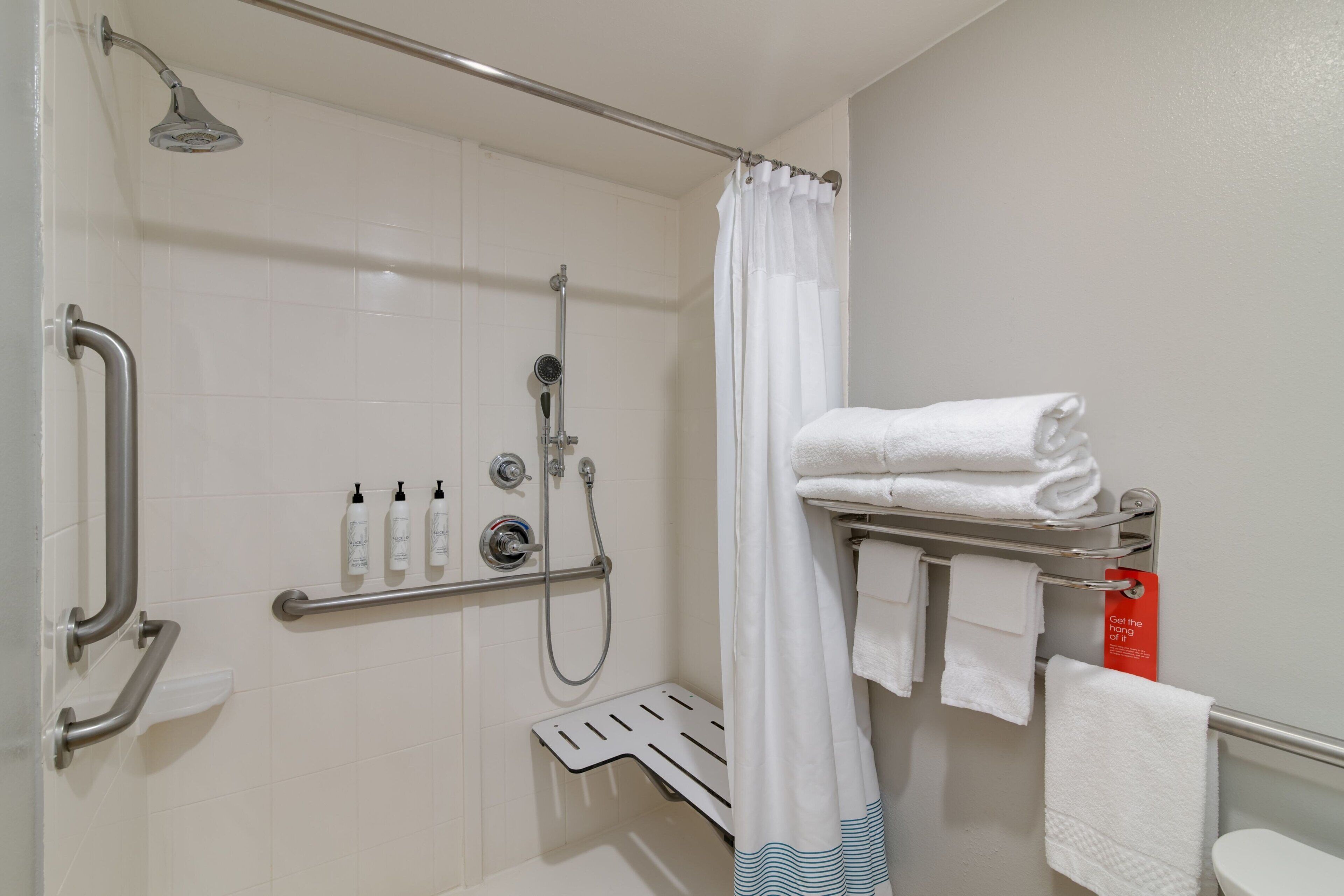 A bathroom with a shower, grab bars, a towel rack, and a toilet.