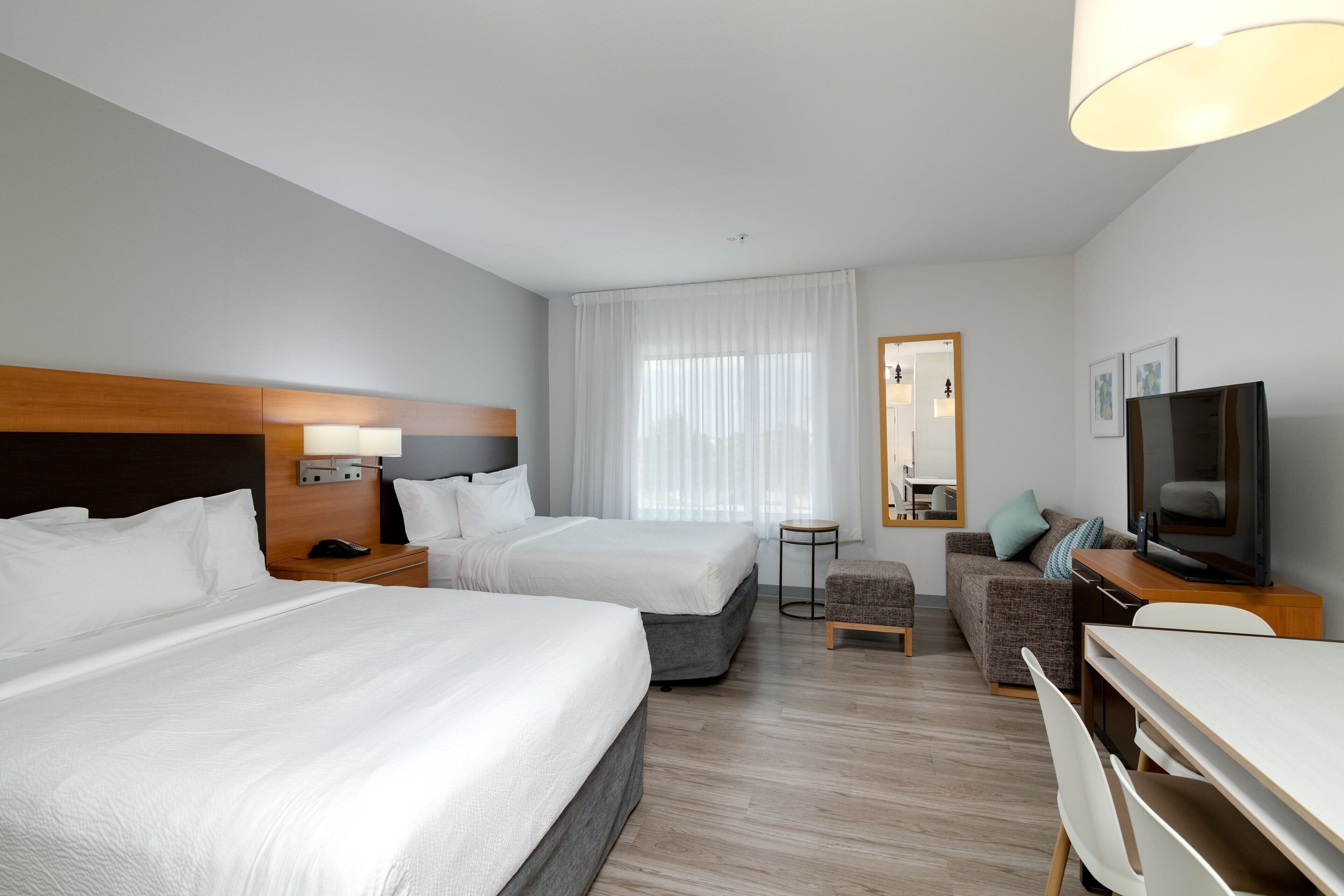 A hotel room with two beds, a desk, a television, and a small seating area.