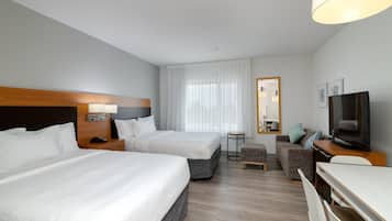 A hotel room with two beds, a desk, a television, and a small seating area.