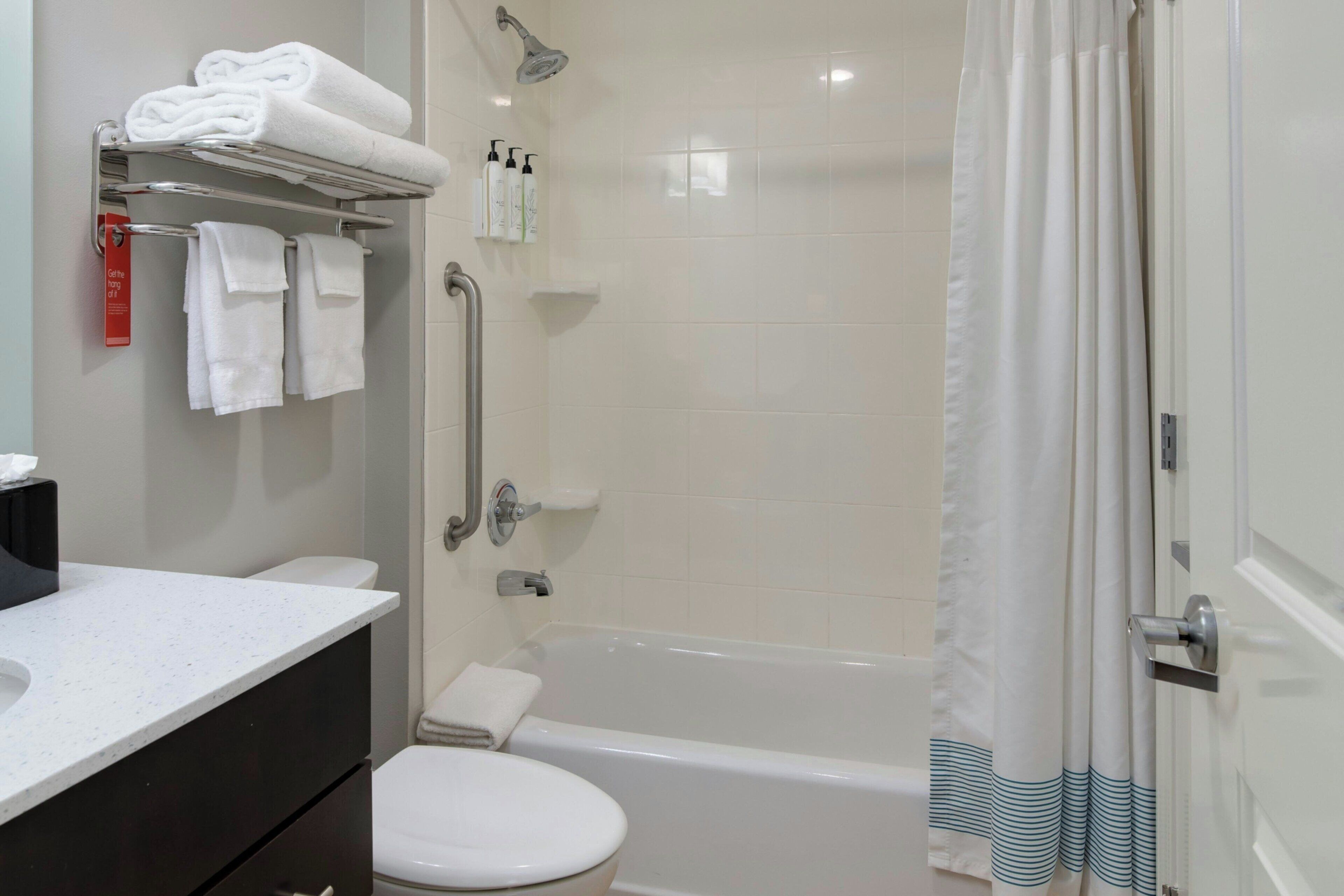 A bathroom with a white toilet, a bathtub, a shower with a handheld showerhead, and a towel rack with folded towels.